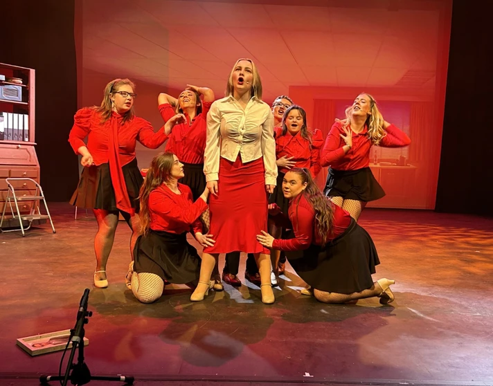 Energetic musical number featuring a group of performers dressed in red, singing passionately on stage. Energetic musical number featuring a group of performers dressed in red, singing passionately on stage.